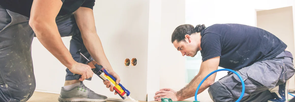 Zwei Personen bringen eine Sockelleiste an.